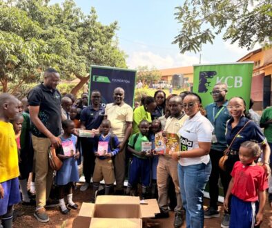 Some of the KCB staff pose for a photo with pupils from St.Jude Primary School as they hold some of the reading material donated by the bank